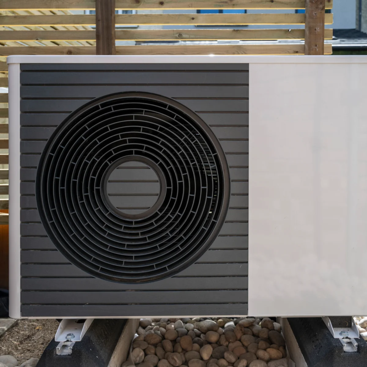 Front view of the air source heat pump outside in the garden, near a wooden fence on a sunny day.