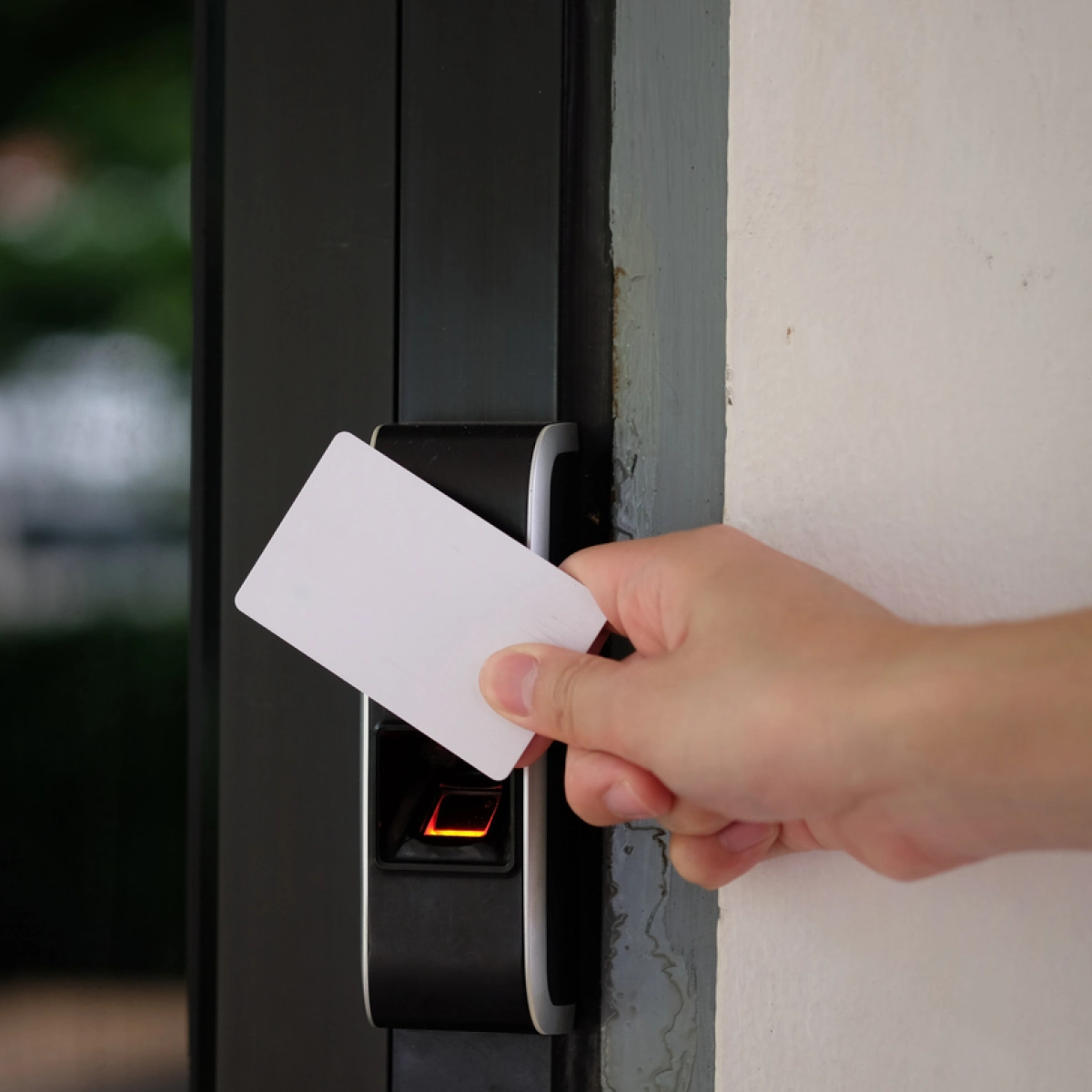 A hand holding a card key up to an electronic door device