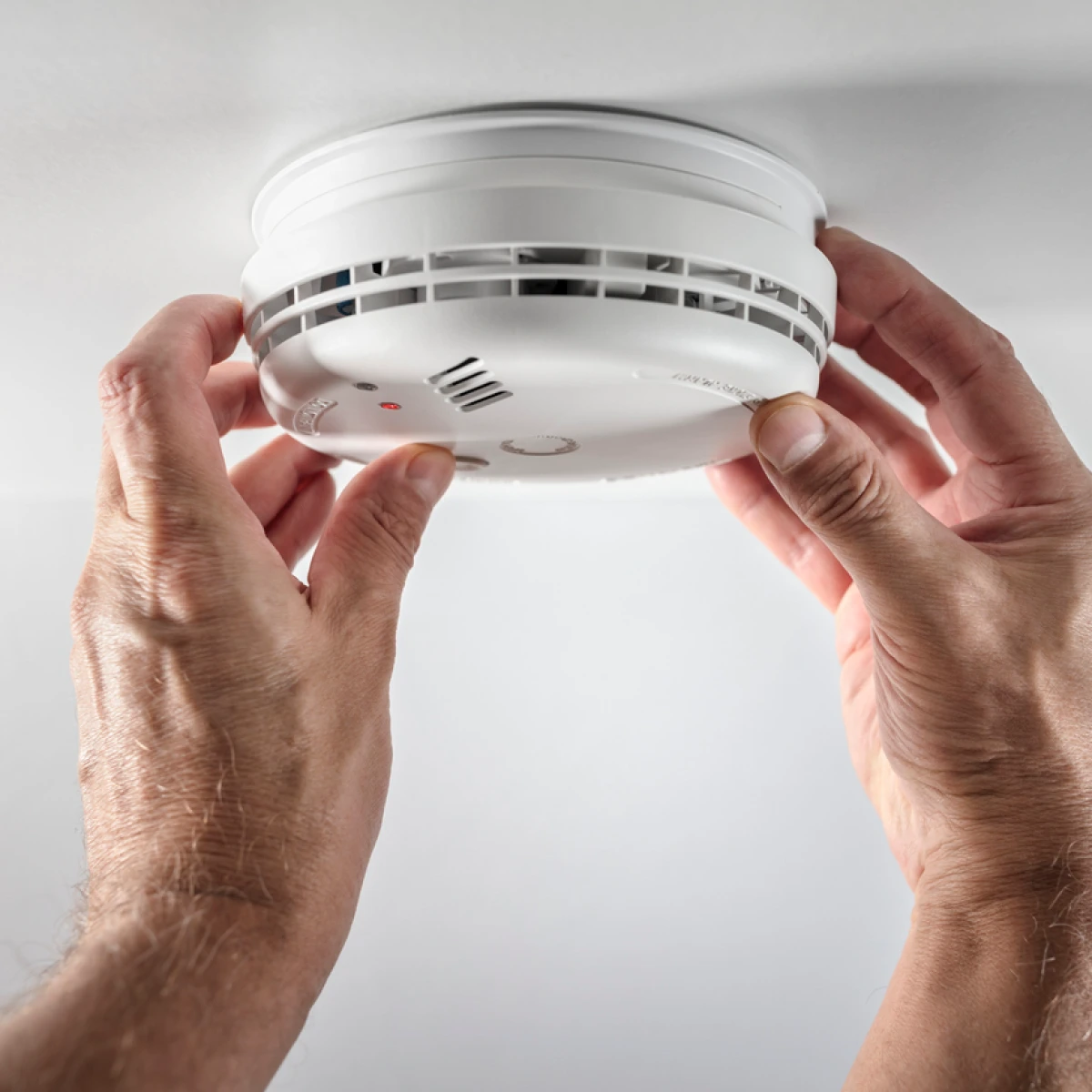 A fire alarm mounted on a white ceiling, with a person