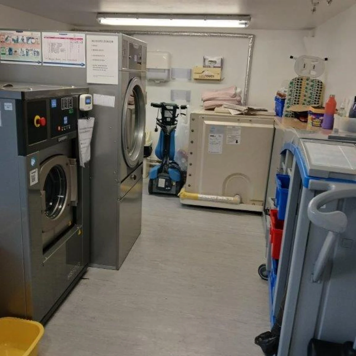 A compact laundry room with grey walls, featuring a washing machine, dryer, and various cleaning supplies