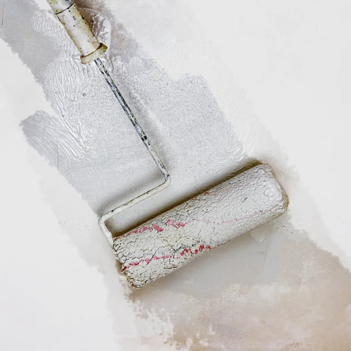 A close up of a paint roller applying fresh grey colour paint onto a white concrete wall.