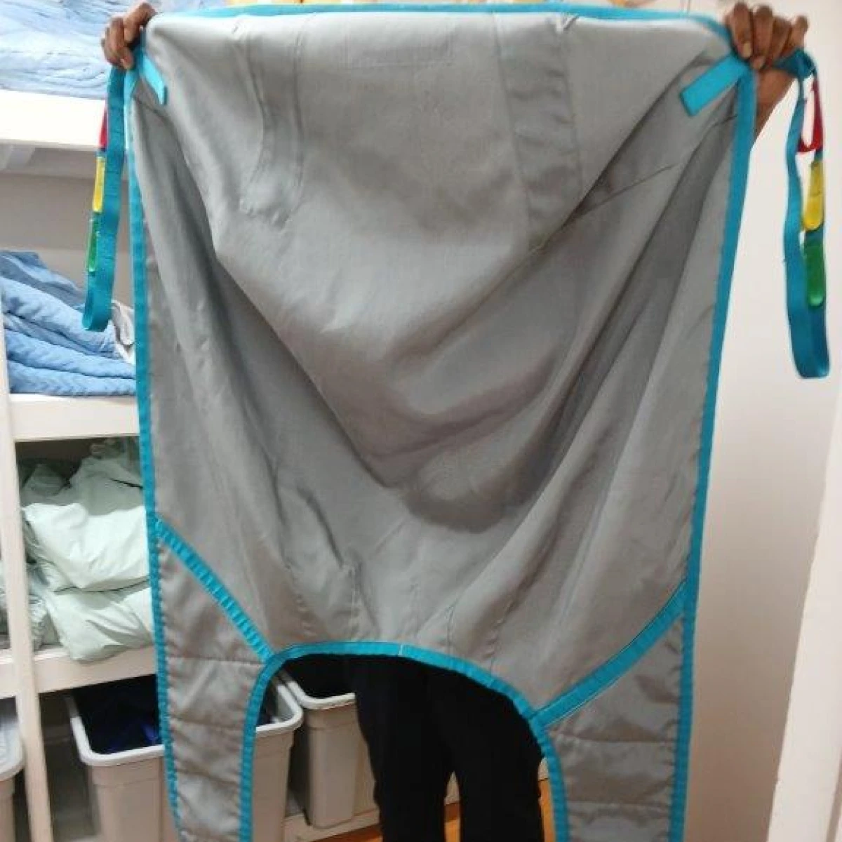 A person is holding up a large grey sling, used to lift and transfer residents